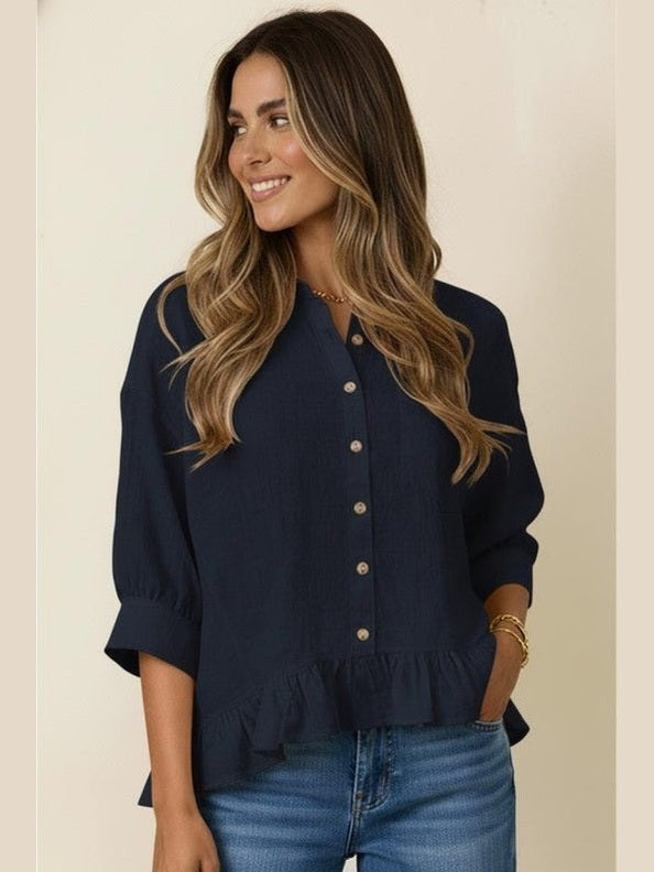 Woman wearing a navy blue blouse with buttons and blue jeans on a beige background